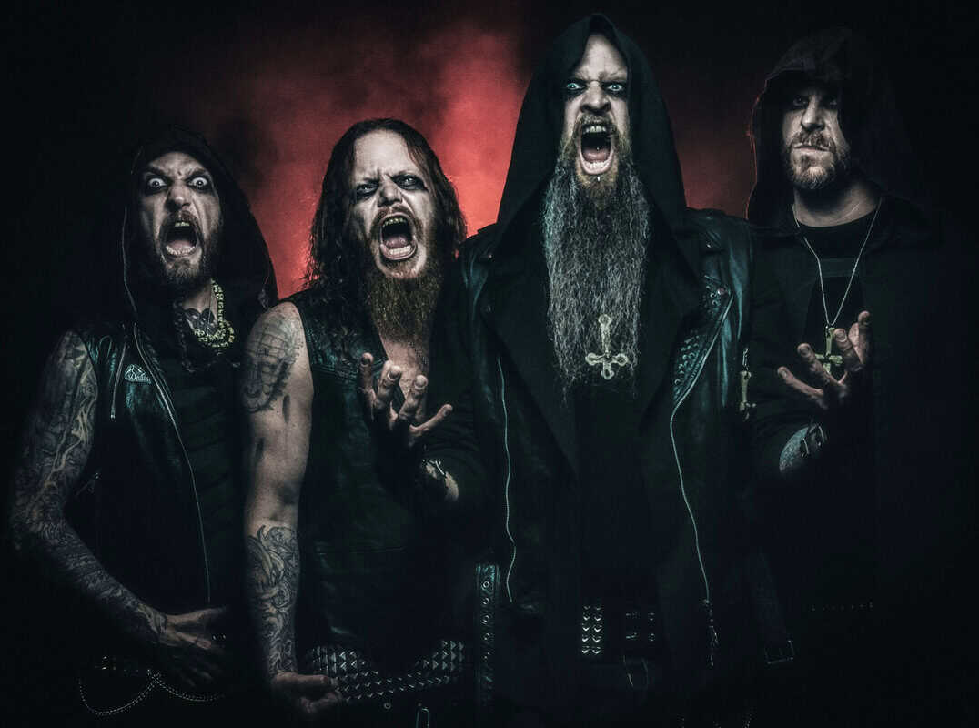 Four male metal musicians in black leather jackets scream toward the camera in a dark, moody setting.