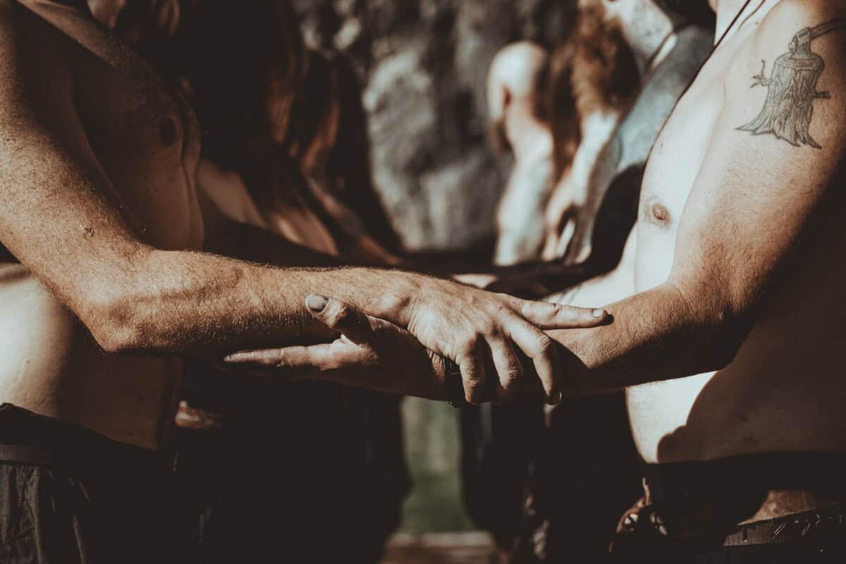 Close-up of intertwined hands and forearms of shirtless people, suggesting unity or solidarity in a circle formation.