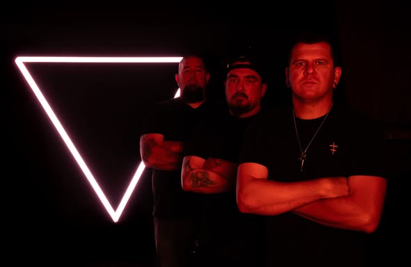 Three men in black shirts pose with arms crossed in a dark studio; a glowing pink neon triangle frames the background.
