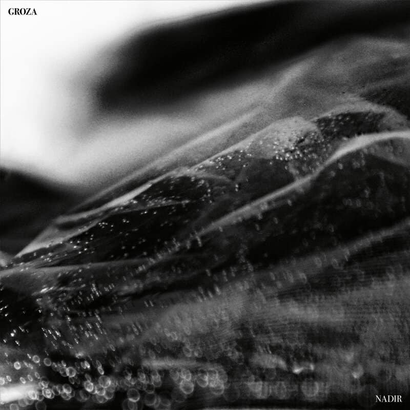 Close-up, black-and-white abstract texture of layered fabric with scattered water droplets and soft bokeh highlights.