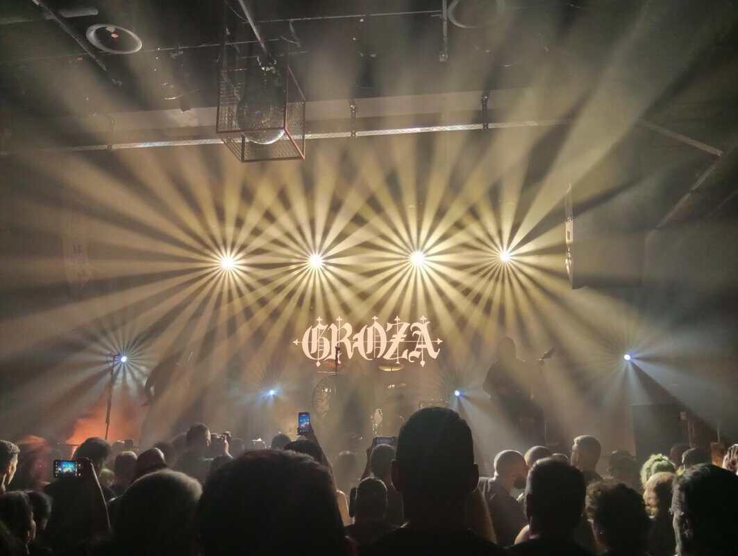 Crowd at a live concert watching a stage with bright radial light beams and a decorative backdrop.