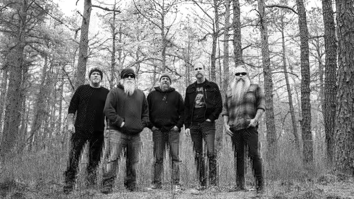 Five men with beards posing together in a wooded forest, front-facing camera in a black-and-white photo.