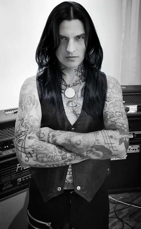 Tattooed man with long dark hair, arms crossed, in a music studio.