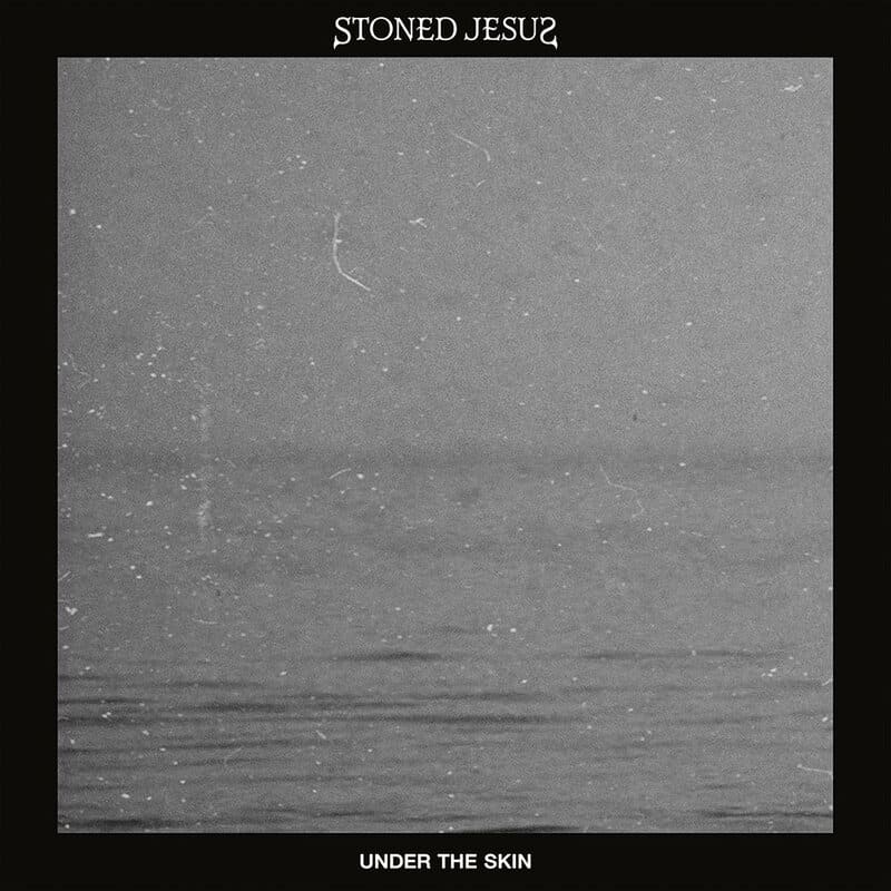 Album cover for Stoned Jesus: Under the Skin, featuring a grainy grayscale landscape with a calm, misty water scene framed by a black border with white text at the top and bottom.